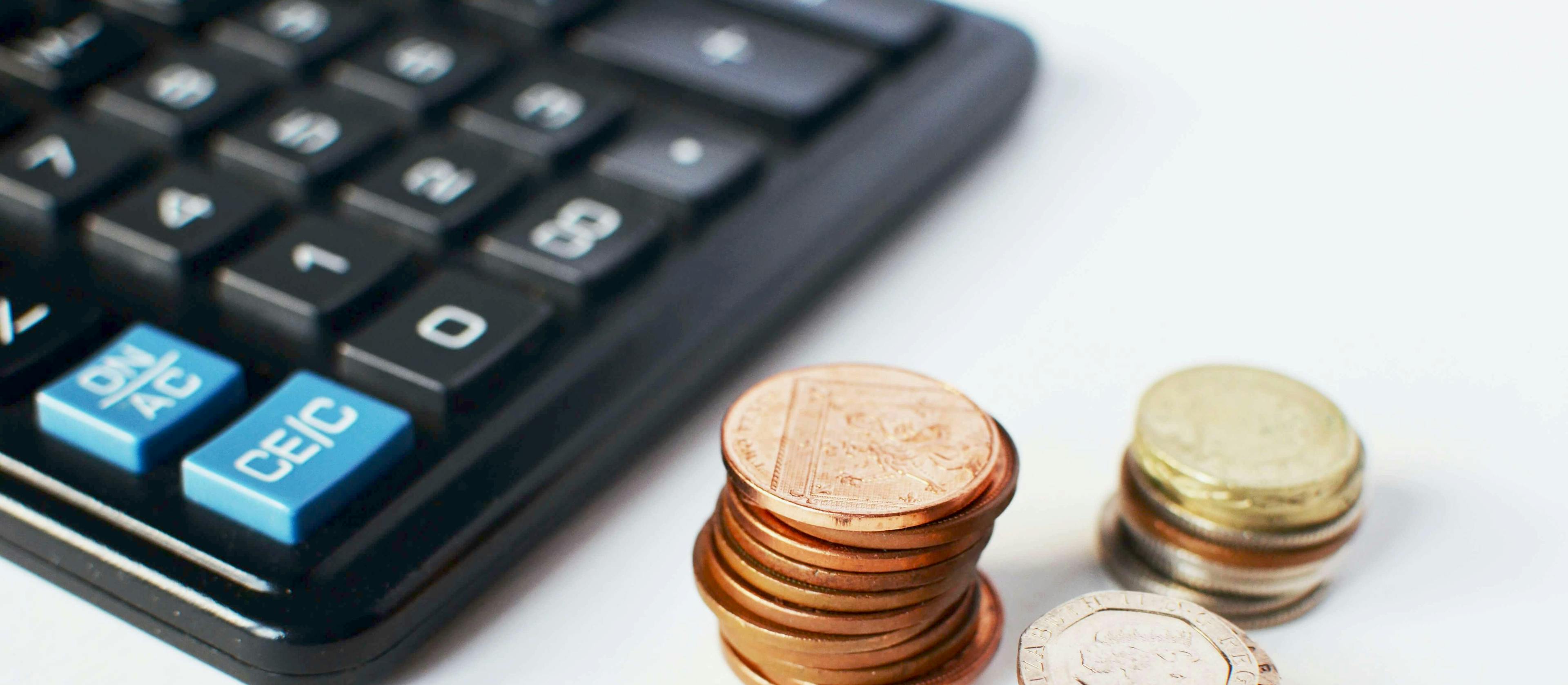 A calculator and coins on a desk where staff have been calculating cost plus pricing for products